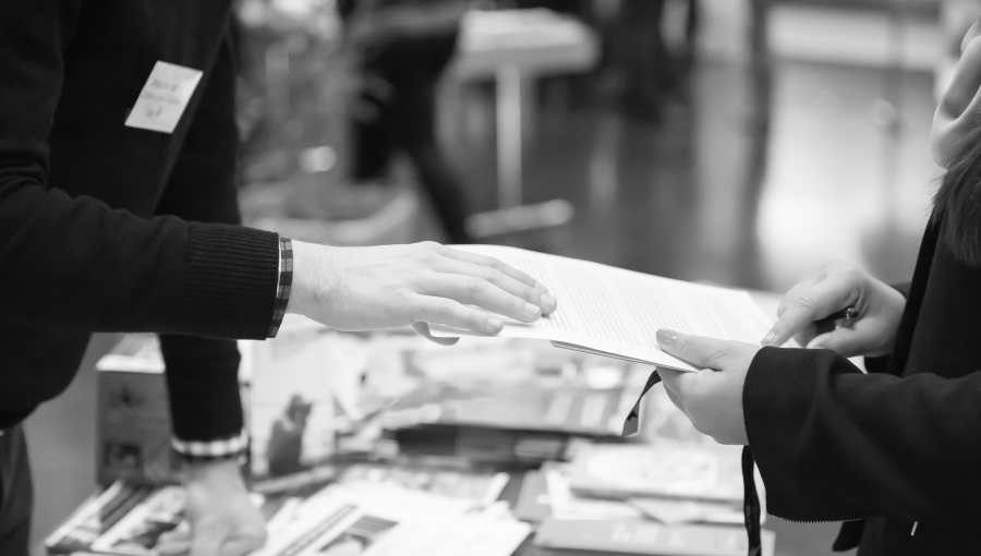 Exhibitor booth attendant handing papers and talking to attendee black and white