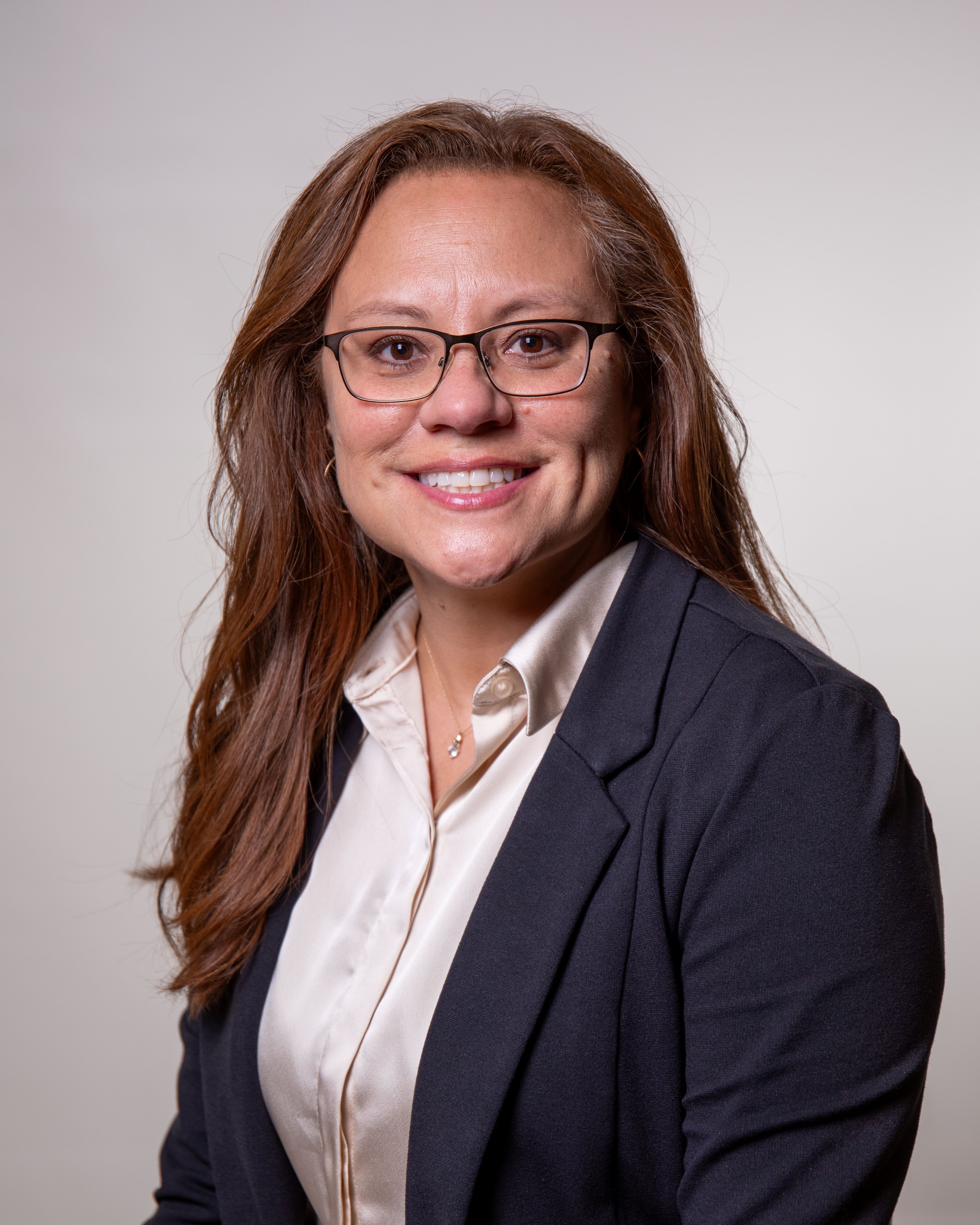 smiling woman with brown hair, wearing a white shirt and a dark blue jacket