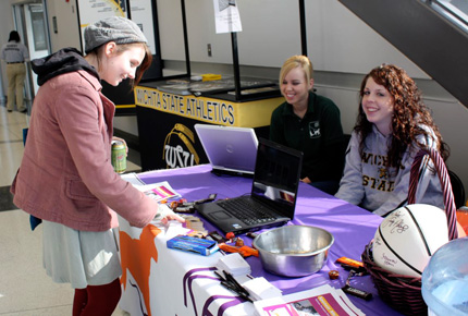 Katie Chrapkowski and Whitney Homan staff a table for the Humane Society at a Shocker women's basketball game, while Anna Bergen learns about the 