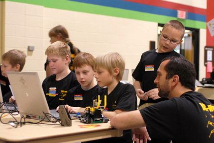 Students cluster around their LEGO-built robot to ensure its performance for competition.