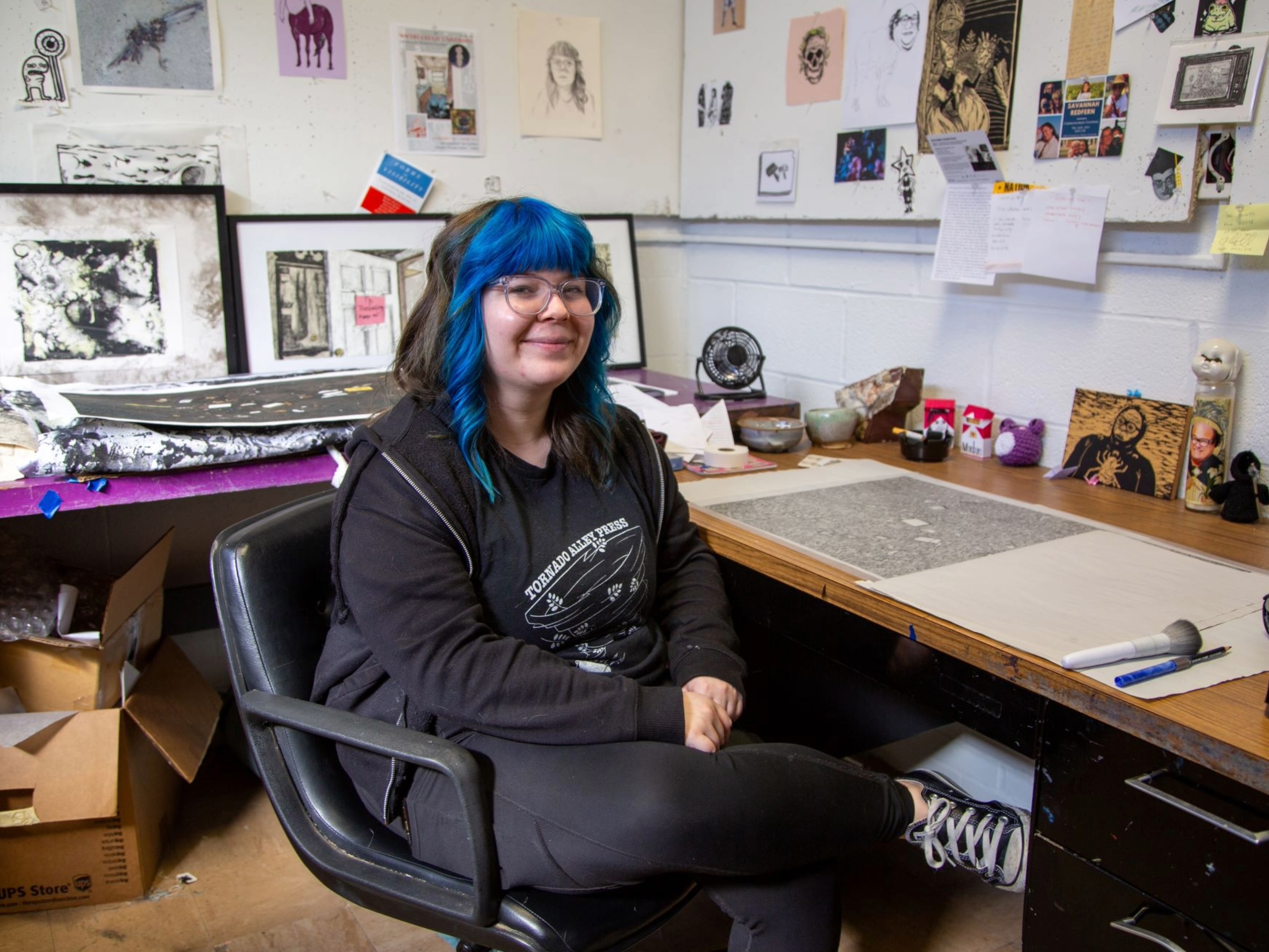 MFA student Zoë Gillis sits in a desk chair in her McKnight Art Center studio surrounded by prints.