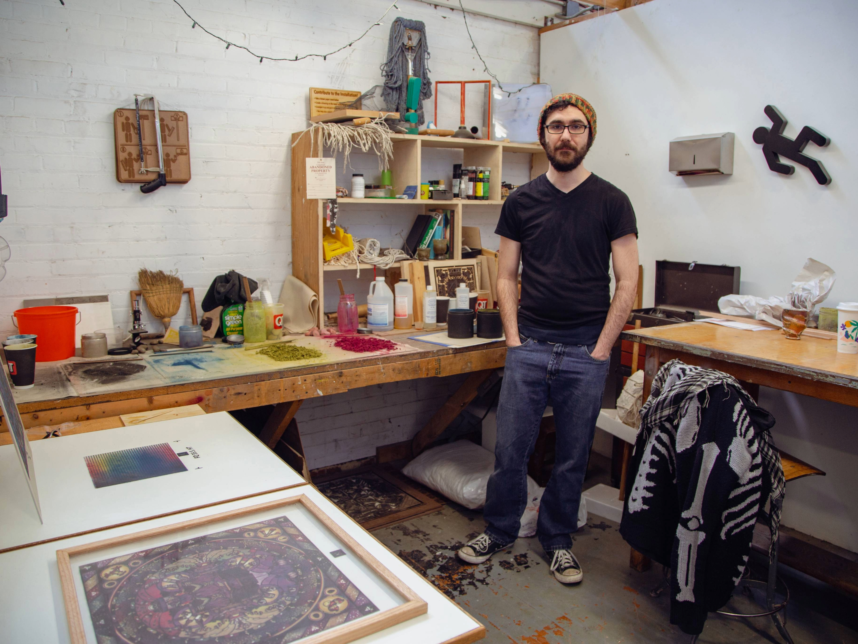 MFA student Anthony Corraro stands, with his hands in his pockets, in his Henrion Hall studio surrounded by art supplies.