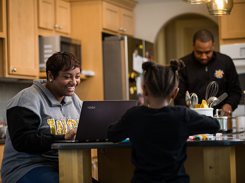 Student working on laptop alongside family