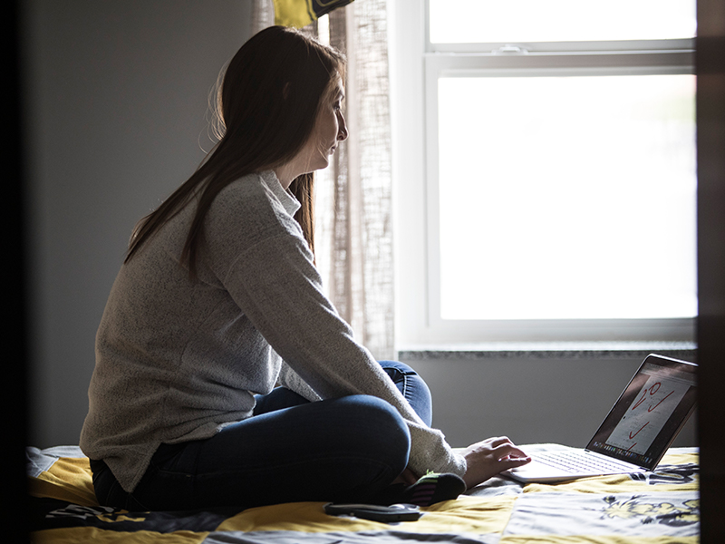 A student sits alone in her dorm room.