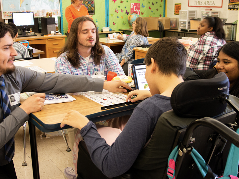 From left to right, WSU engineering students Jacob Lewis, Brendan Lajza and Meghana Ravi assist Katlyn with the use of her new stylus and optimized Proloquo2Go software.