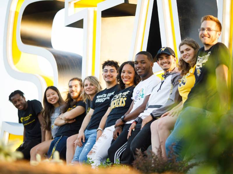 WSU students sitting on a sign outdoors