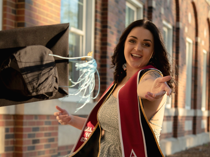 Photo of Mary Elizabeth Thornton tossing her graduation cap towards the camera.