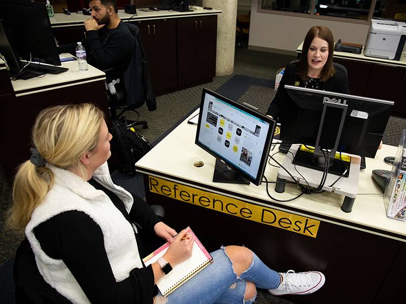 Student and librarian sitting across a reference desk from each other. 