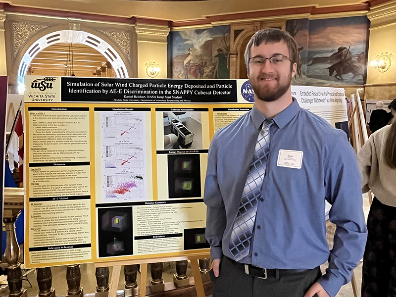 Daniel Reichart poses in front of his research poster at the Kansas state capitol 