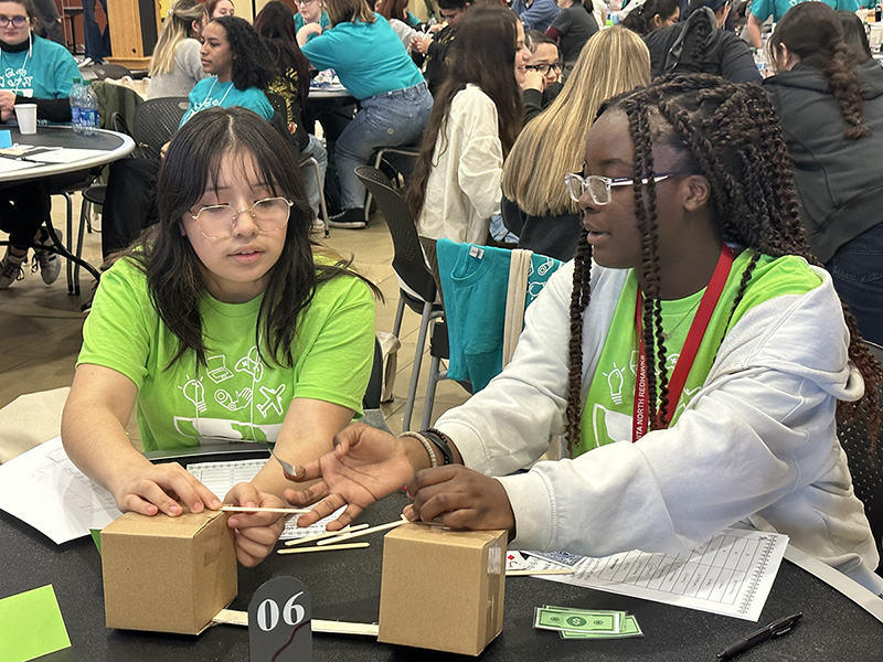 Two girls sit at a table with game pieces in front of them. 