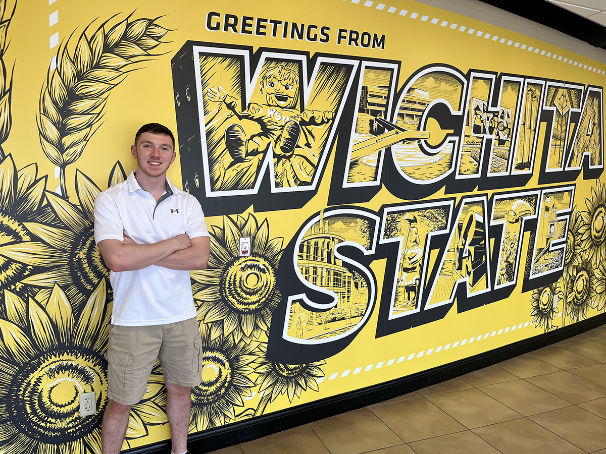 Carter Duff stands next to a Wichita State mural