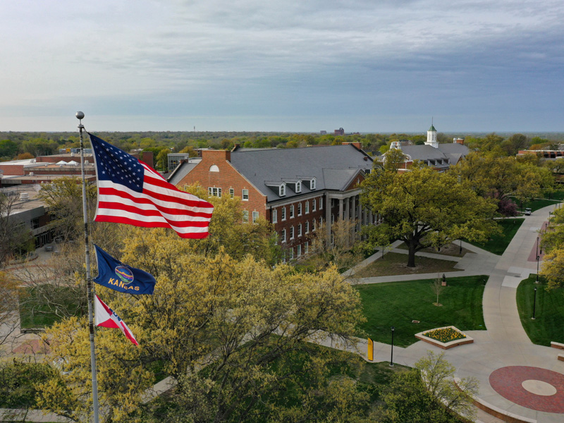 Overhead photo of campus with a flag pole with the United States, Kansas and Wichita flags in the foreground and the campus in the background