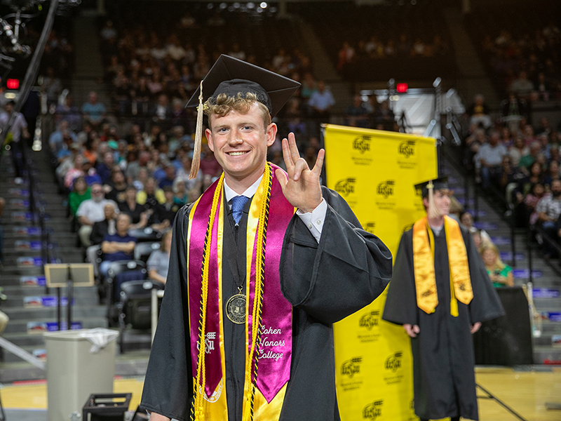 A graduate holds up the Shocker hand sign