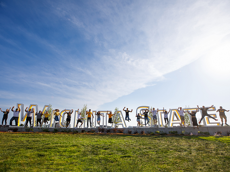 Wichita State students pose and jump near a Wichita State sign. 