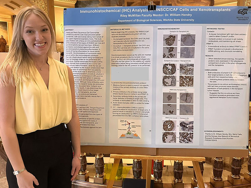 Riley McMillan poses in front of her research poster at the Kansas state capitol