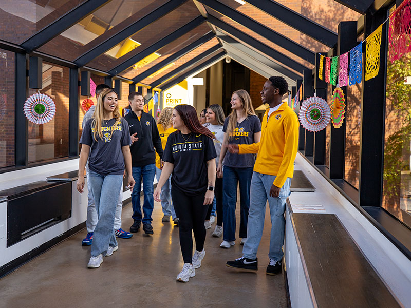Wichita State students walk through a windowed hallway. 
