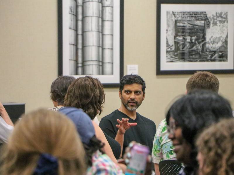 Faculty sit and stand around tables in discussion at the FARE end-of-semester celebration