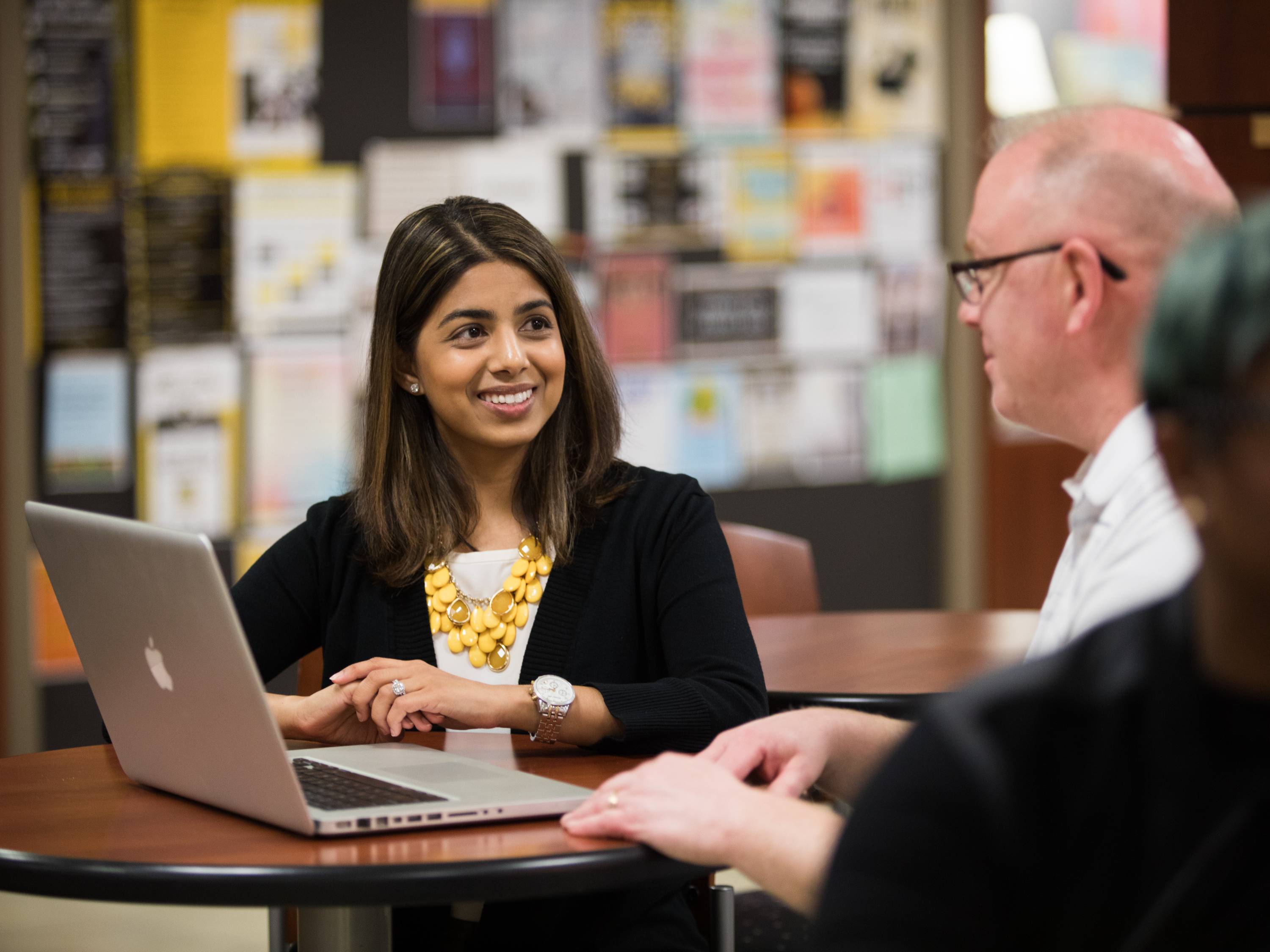 A woman at a laptop talks with a man