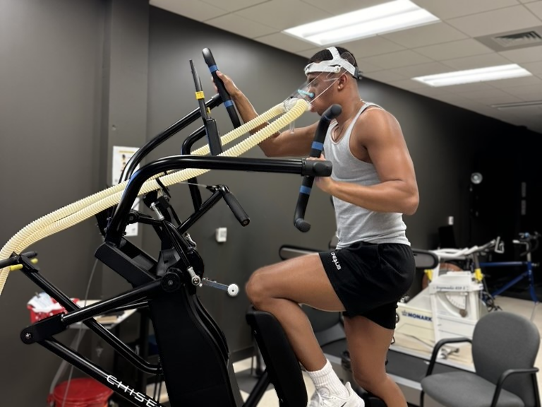 Student wearing a respiratory mask undergoes a VO2 max test on an exercise machine.