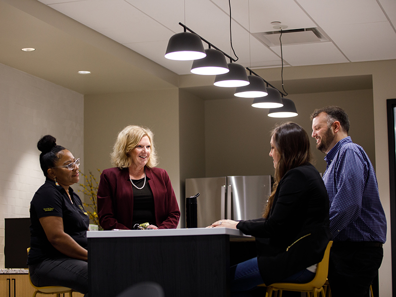 Four faculty gather aroun d table in a Woolsey Hall lounge space