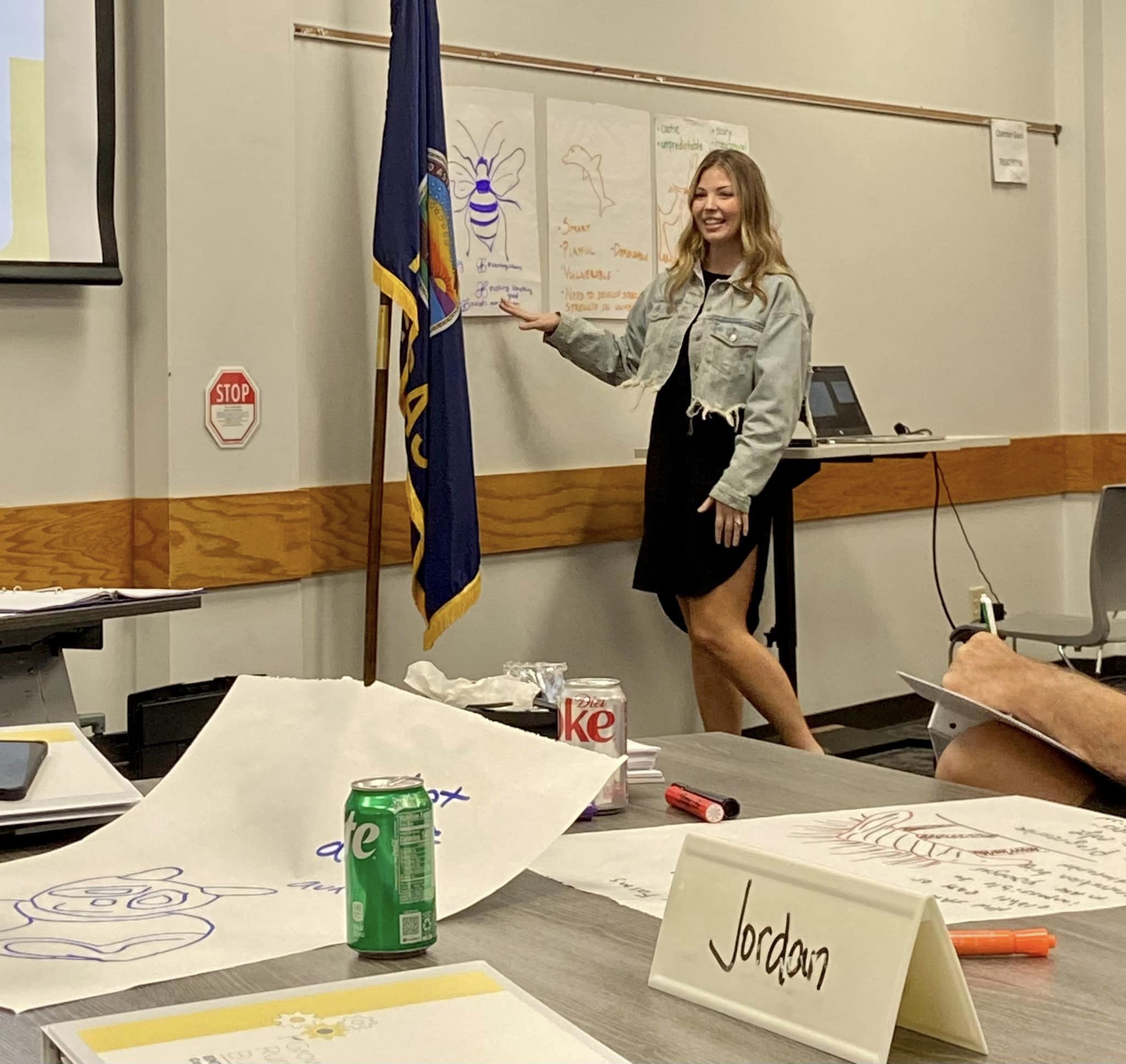 A trainer speaks to participants while pointing to a poster