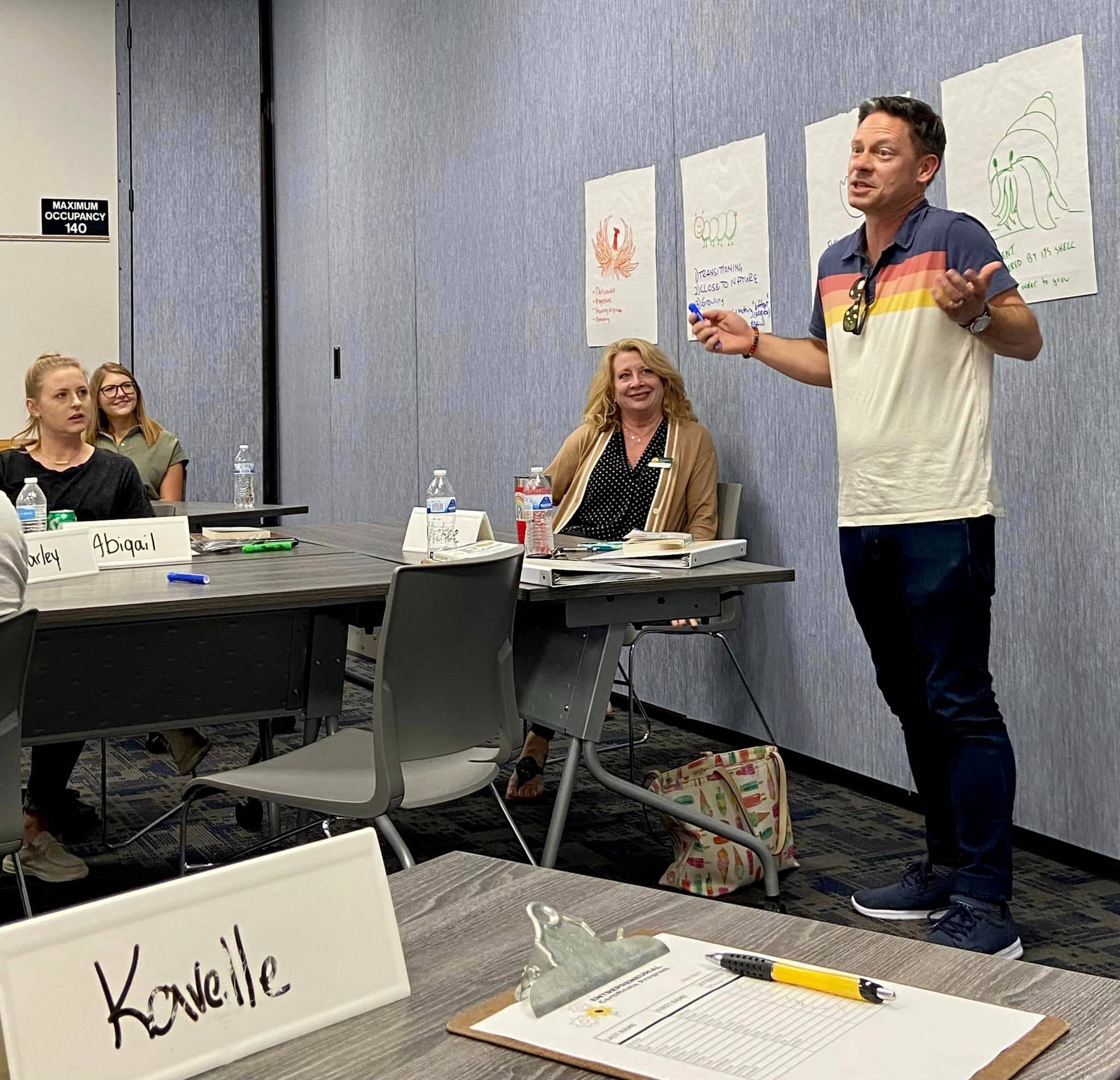 A trainer is speaking to a group of participants as they all look at him.