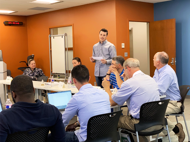Man speaking to others in a class while they listen. 