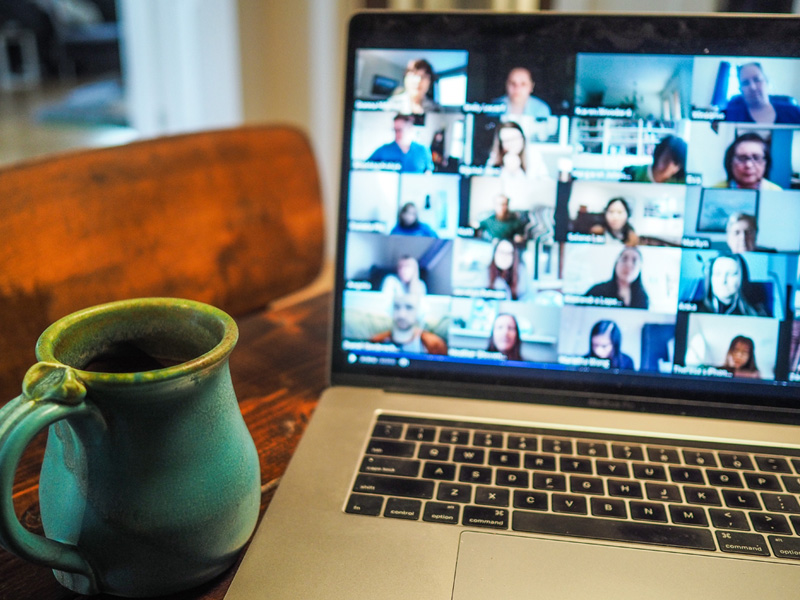 A computer with a zoom call pulled up. Next to it is a green mug.