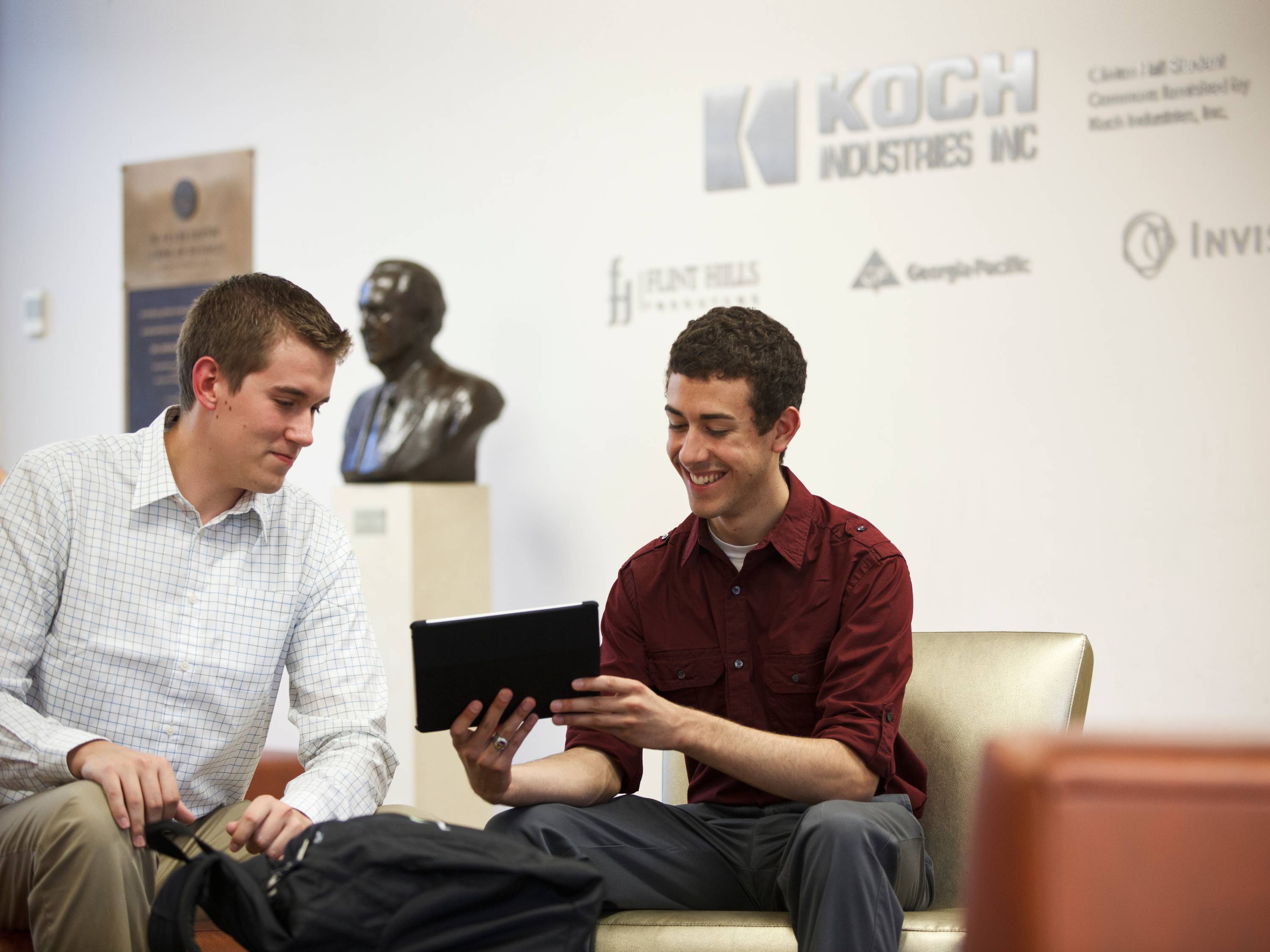A photo of two students smiling at something on a tablet device. 