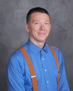 Photo of Dr. Armstrong smiling, wearing a blue shirt with suspenders