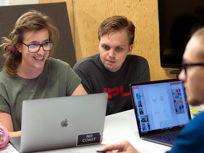 Three students gather around laptops