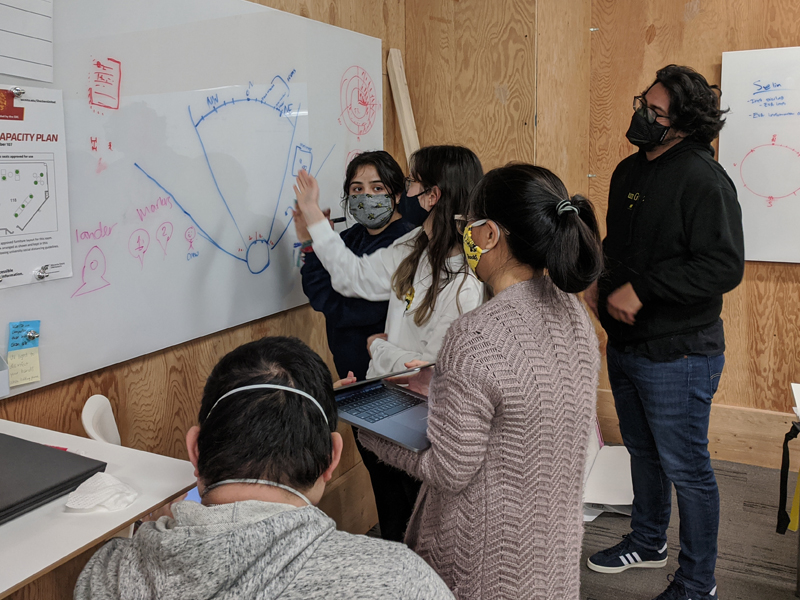 Five students brainstorm together at white board for NASA SUITS design competition