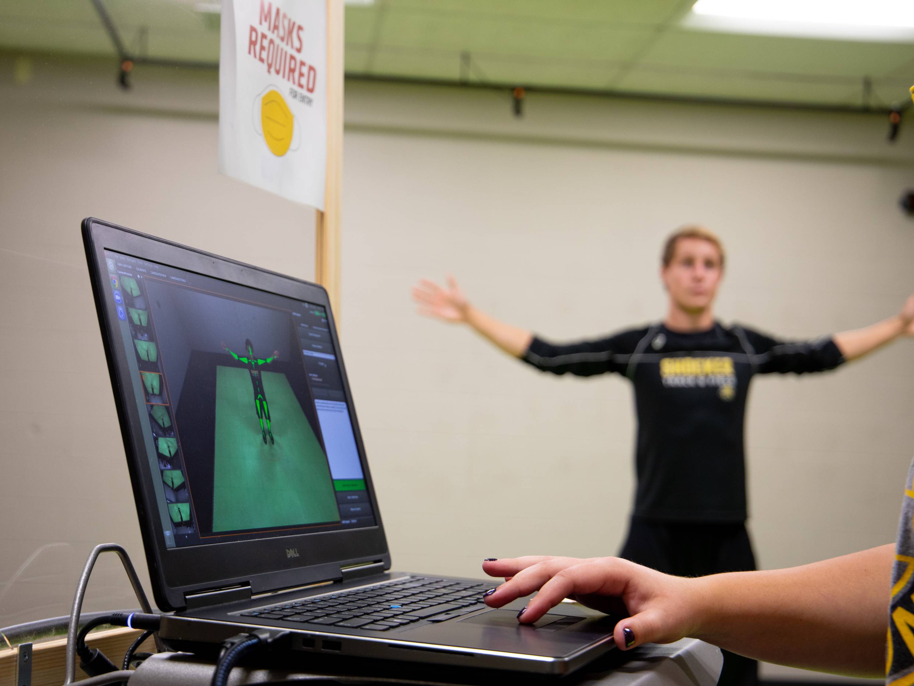 Student performing a motion capture exercise while data is displayed on a laptop screen during a demonstration in the Human Performance Lab.