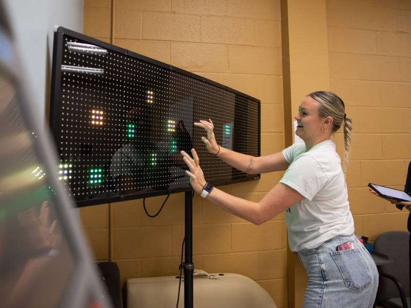 A student interacts with a LED light board, tapping colored lights that appear on the board. 