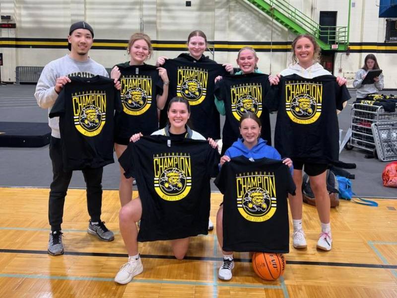 Students from the Wichita State Athletic Training Student Association pose in a gym while hoding up shirts that have WuShock and the text "International Champion".