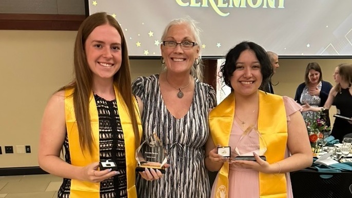 Faculty member, Heidi VanRavenhorst-Bell, smiles for a picture with two departmental honors students holding awards.