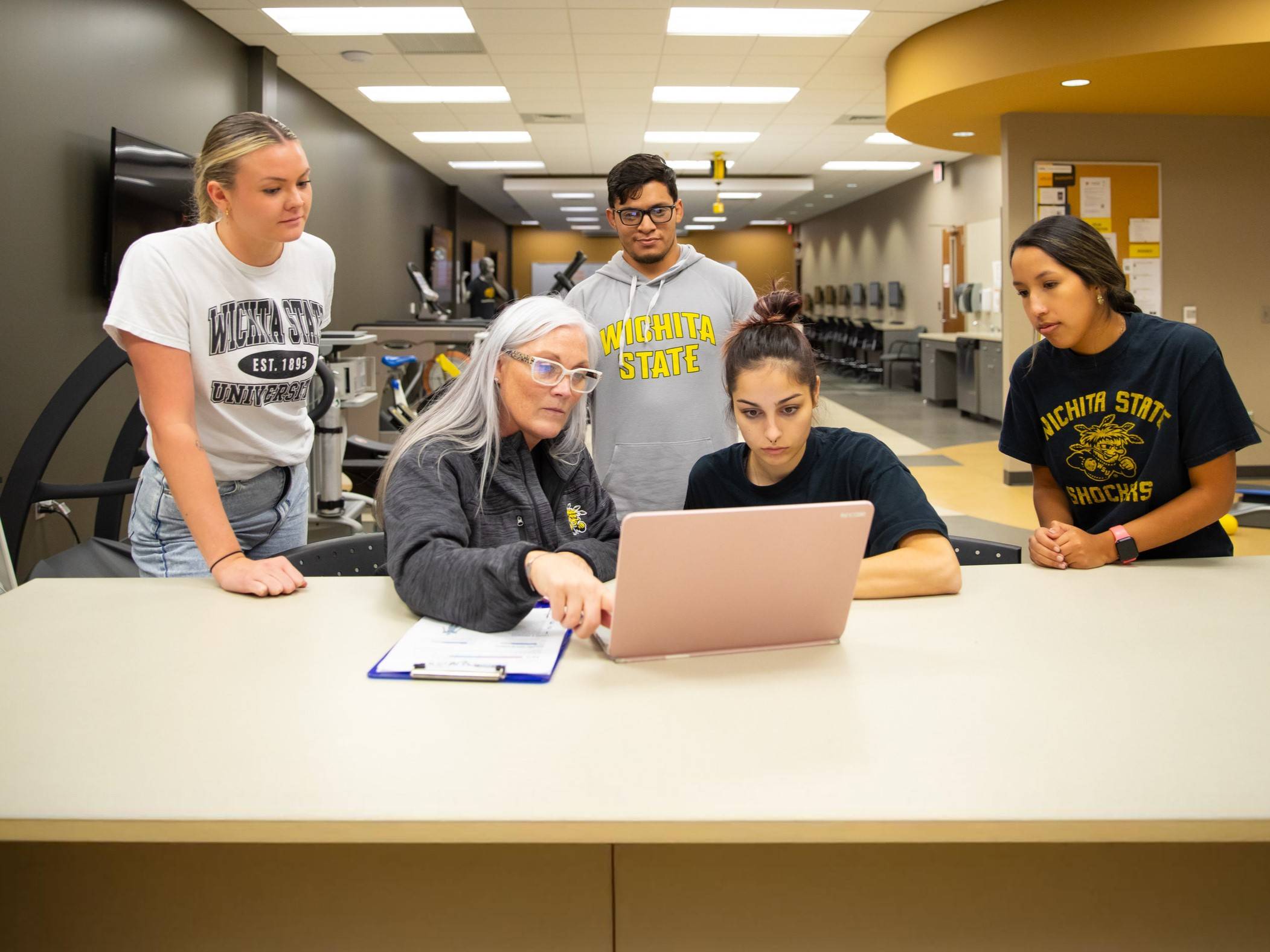Student working on a laptop with instruction from faculty member while three other students look over her shoulder.
