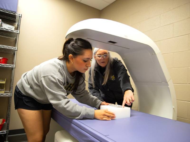 Student positioning an object on a scanning bed while instructor points to guide her.