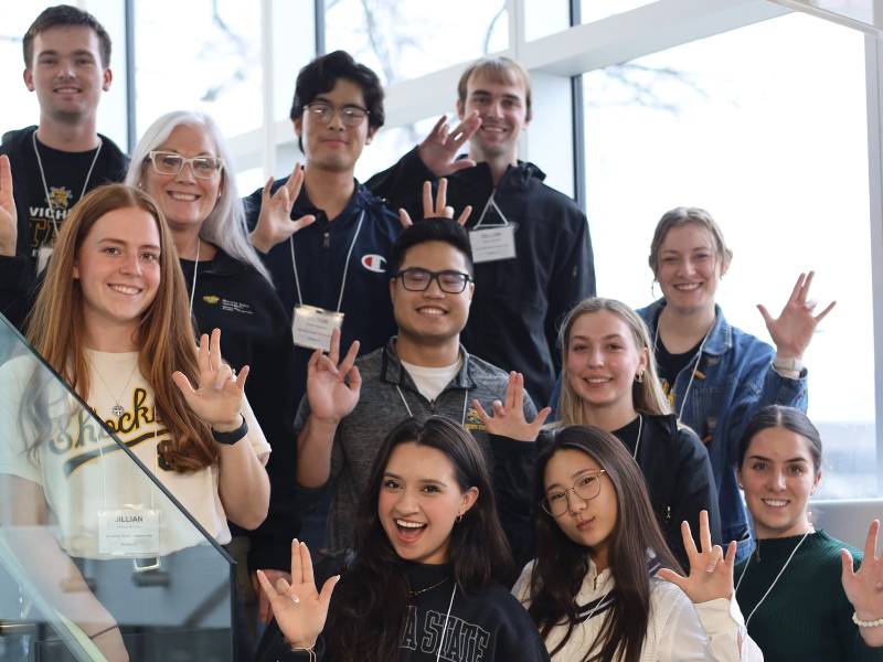 Students from the Exercise Science Student Organization pose on a staircase at a conference holding up "WuShock" hand gesture.
