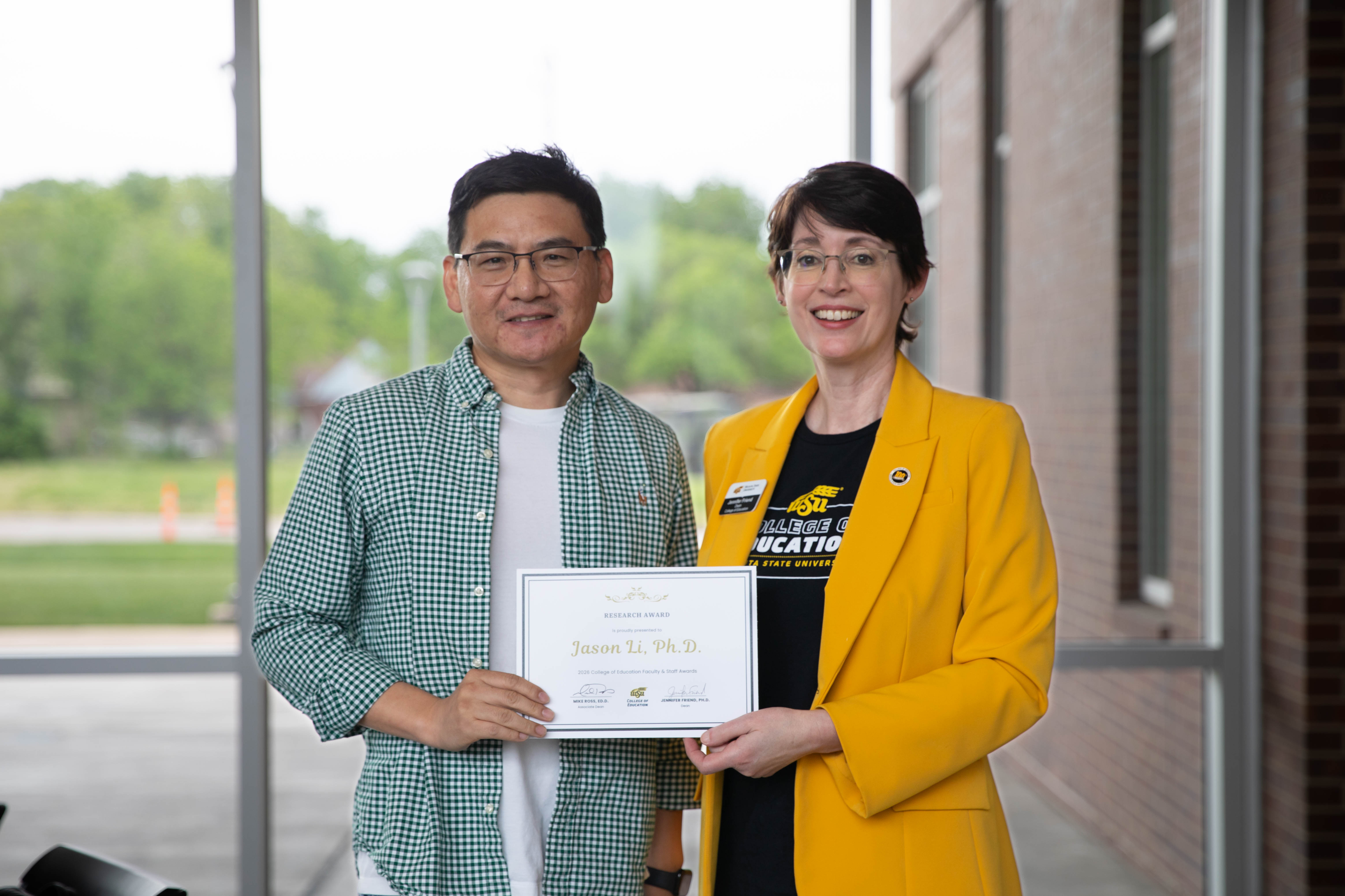 Dr. Jason Li holds a research award certificate while standing with Dr. Jennifer Friend, dean of the College of Education.