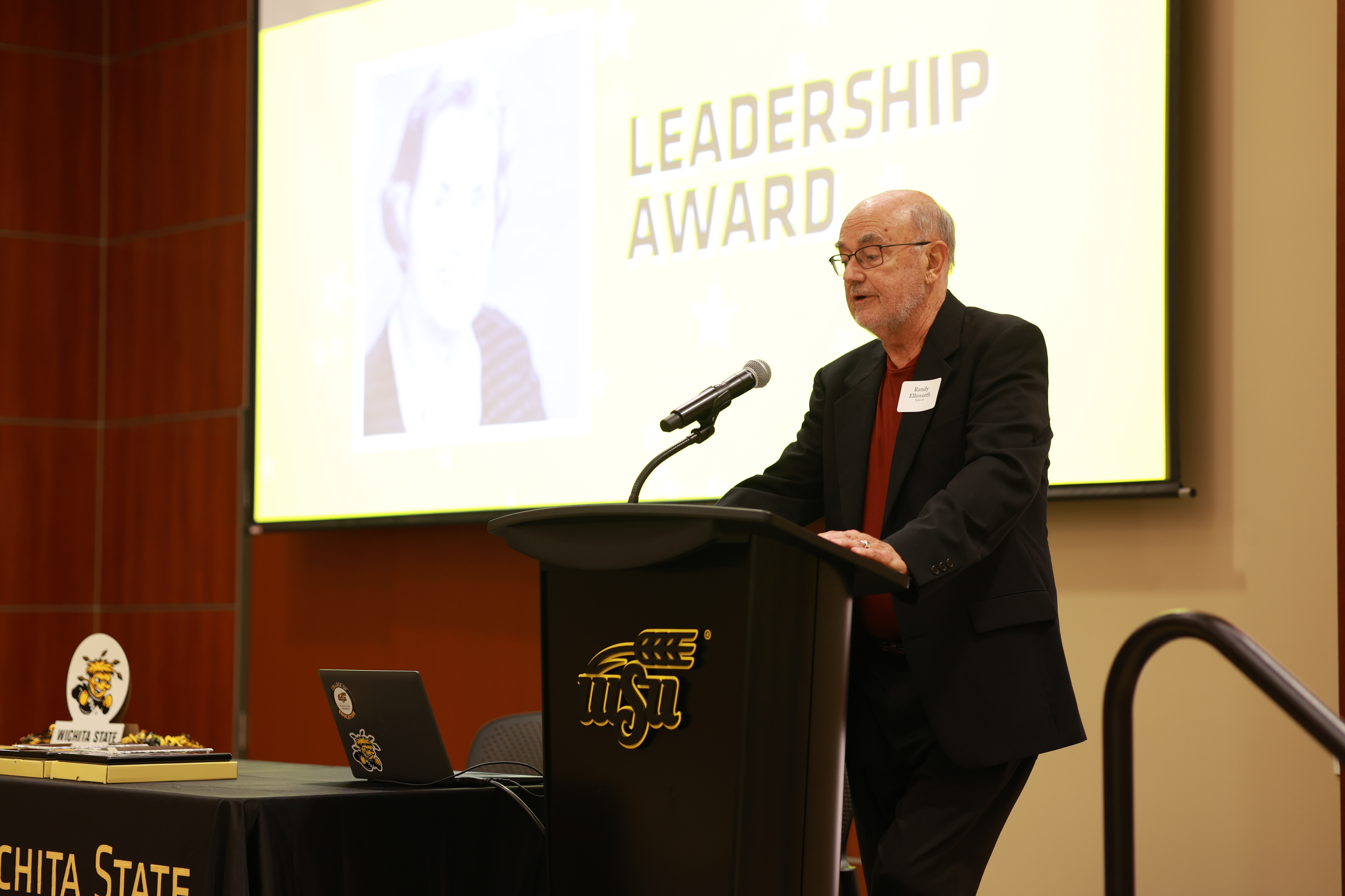 Randy Ellsworth speaks at the podium while accepting the Leadership Award on behalf of Dr. Maurine Fry during the 2026 College of Education Hall of Fame ceremony.
