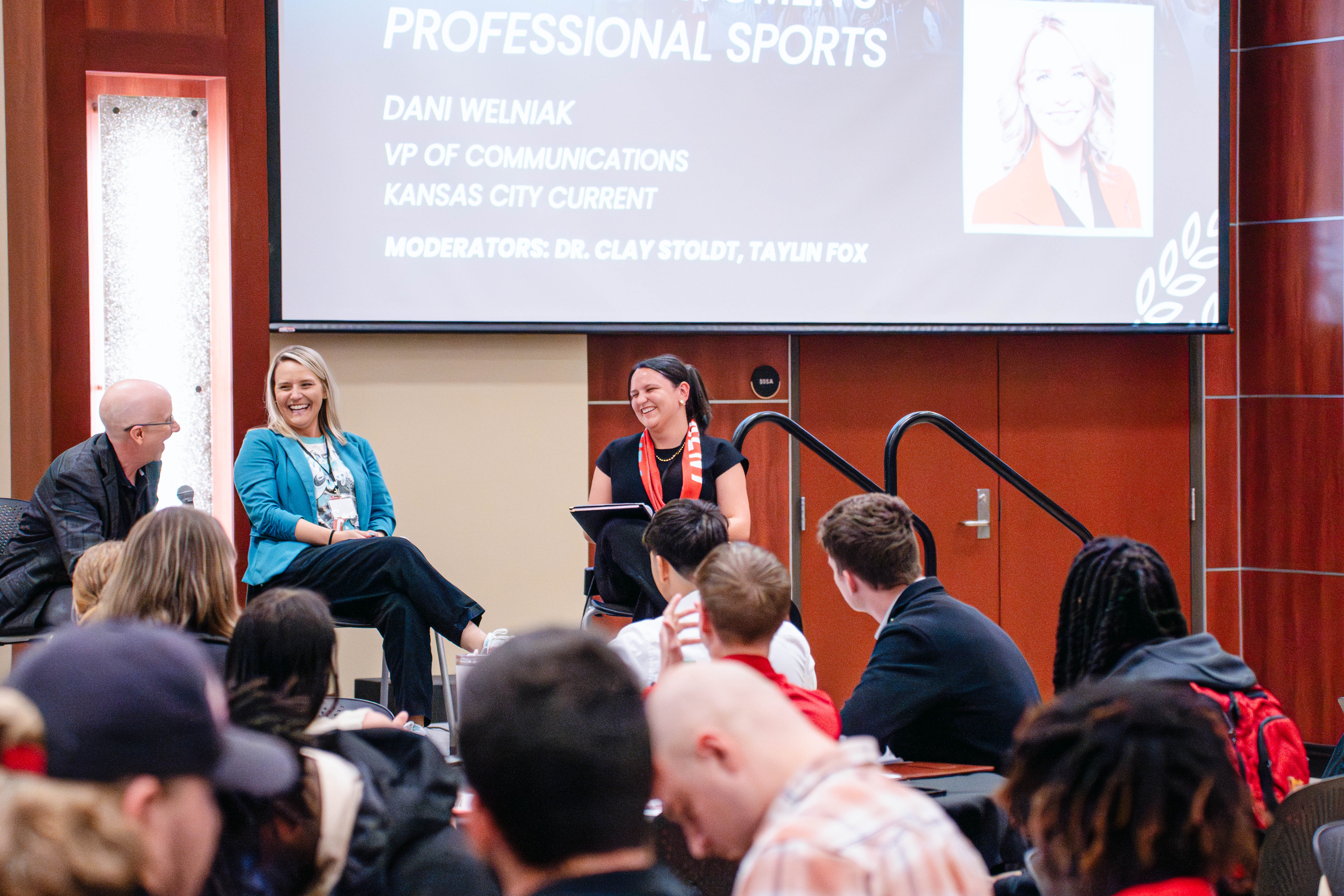 Panelists, including Dani Welniak, speak during a roundtable session at the Kansas Sport Summit at Wichita State University, with attendees seated and listening in a conference room.