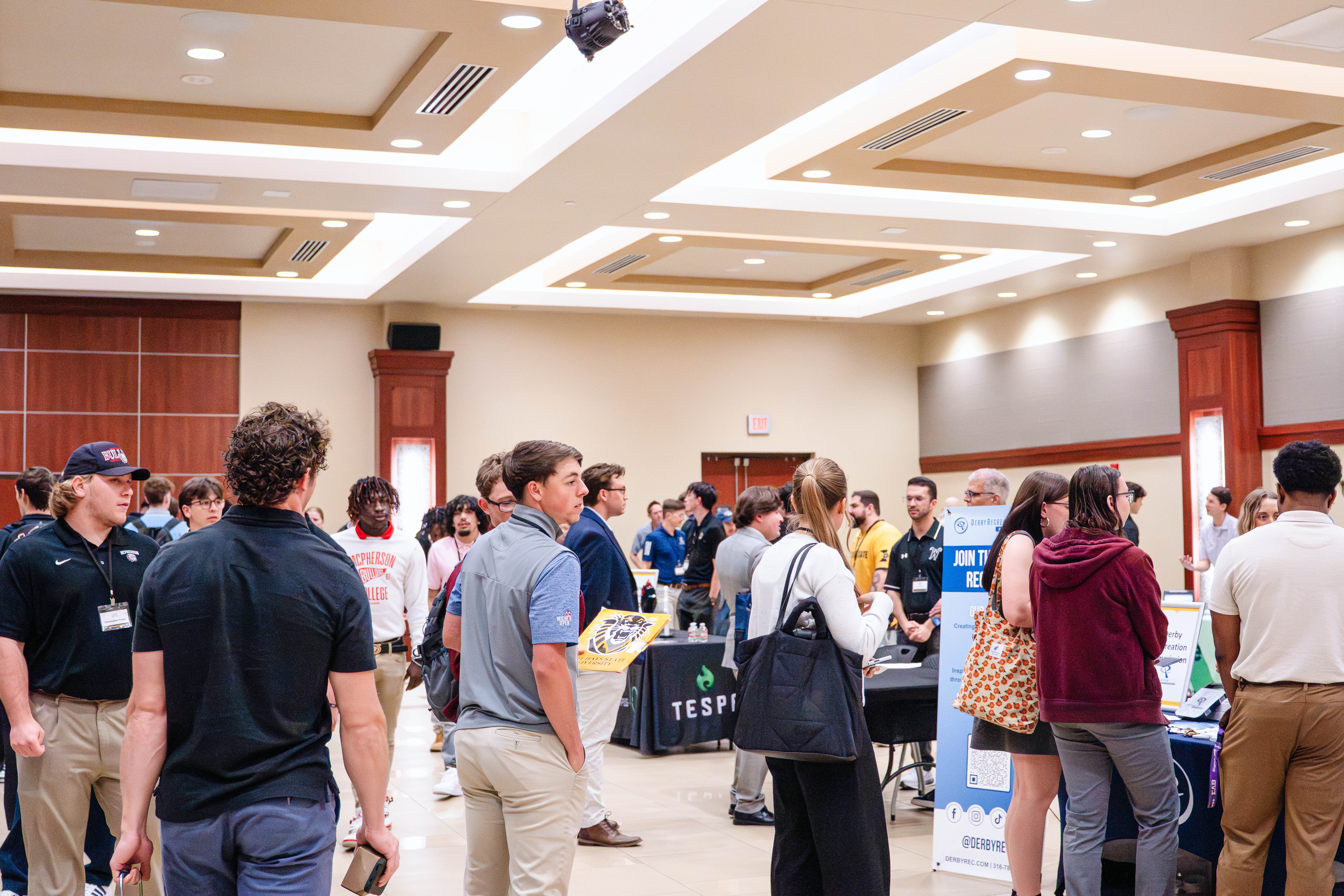 Students and professionals interact with recruiters at tables during the Kansas Sport Summit at Wichita State University, gathered in a conference room with booths and informational displays. Photo by Teresa Vu, Wichita State student minoring in sport management.