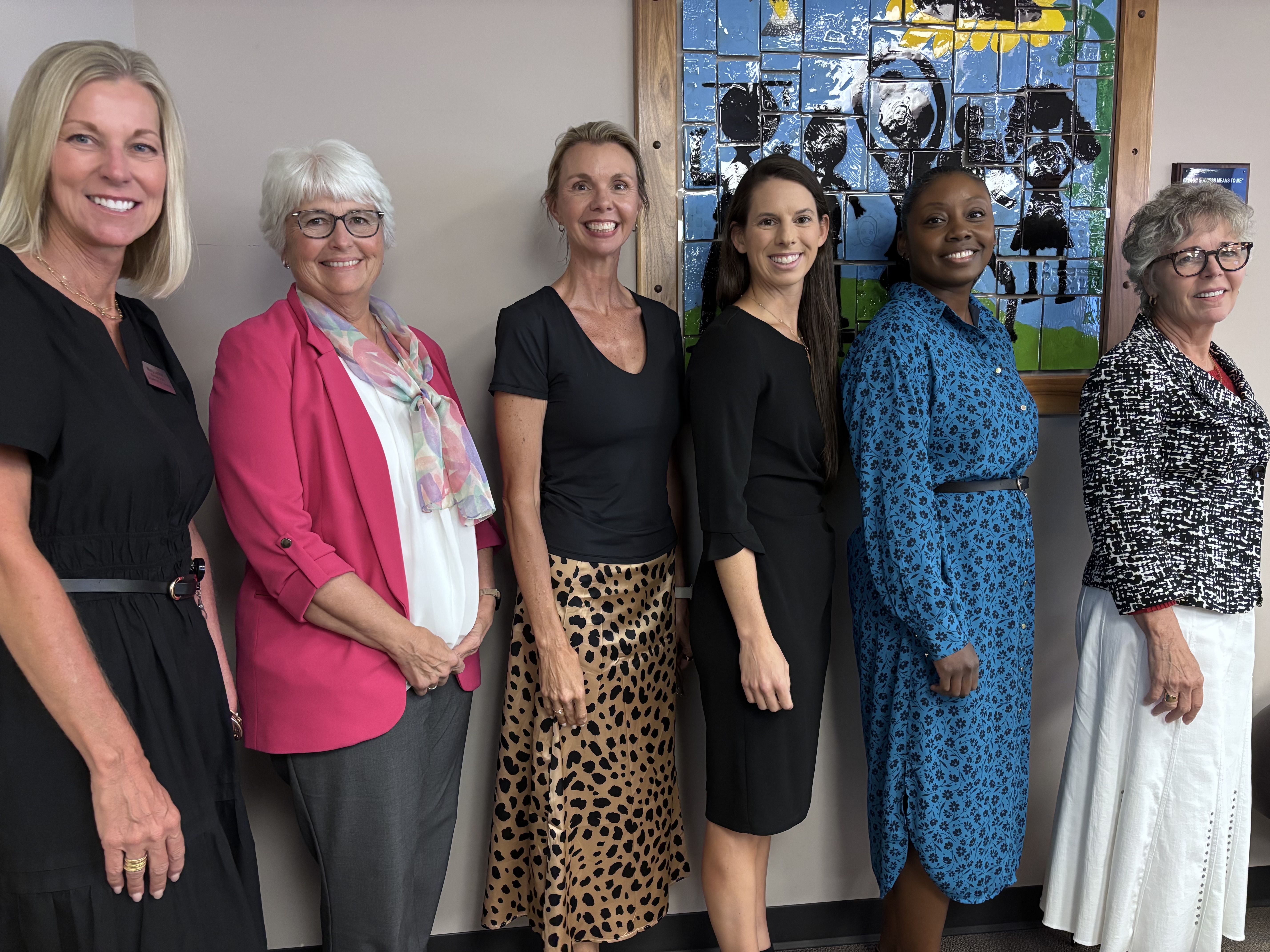 Six women stand together indoors, smiling at the camera in front of a colorful stained-glass artwork. From left are Mary Lonker, English Language Arts Program Manager for Teaching and Learning at the Kansas State Department of Education; Dr. Laurie Curtis, Assistant Director of Teaching and Learning – Structured Literacy at KSDE; Dr. Kim Moody, professor, structured literacy coordinator and director of CLEAR at Wichita State University; Dr. Reagan Murnan, assistant professor of special education at Wichita State; Dr. Sherrie Frazey, executive director of School Support and Improvement for Wichita Public Schools; and Dr. Cindy Lane, director of the Kansas Blueprint for Literacy.
