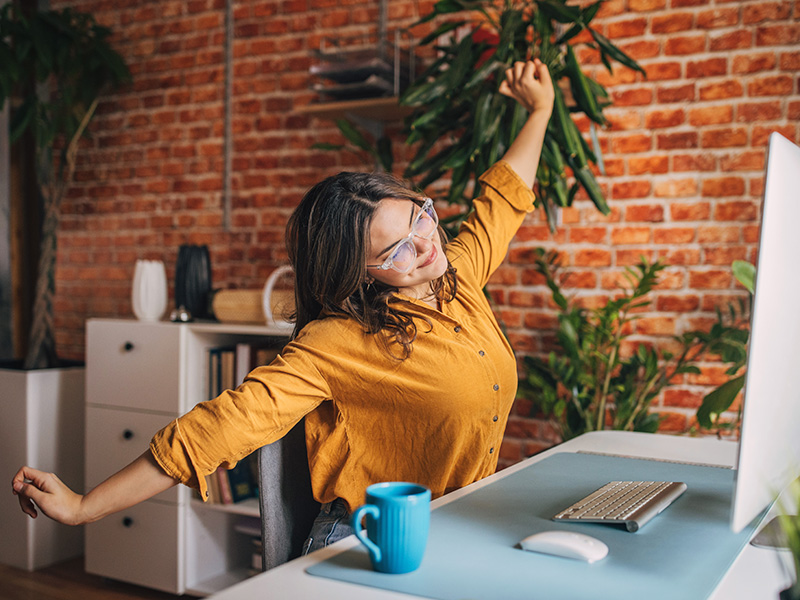 Corporate professional stretching and happy at her desk.