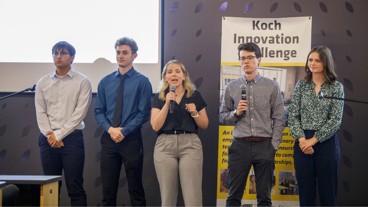 A team of five members deliver an elevator pitch to an audience.