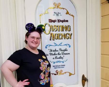 Woman in Mickey Mouse ears poses next to Casting Agency sign at Walt Disney World Resort