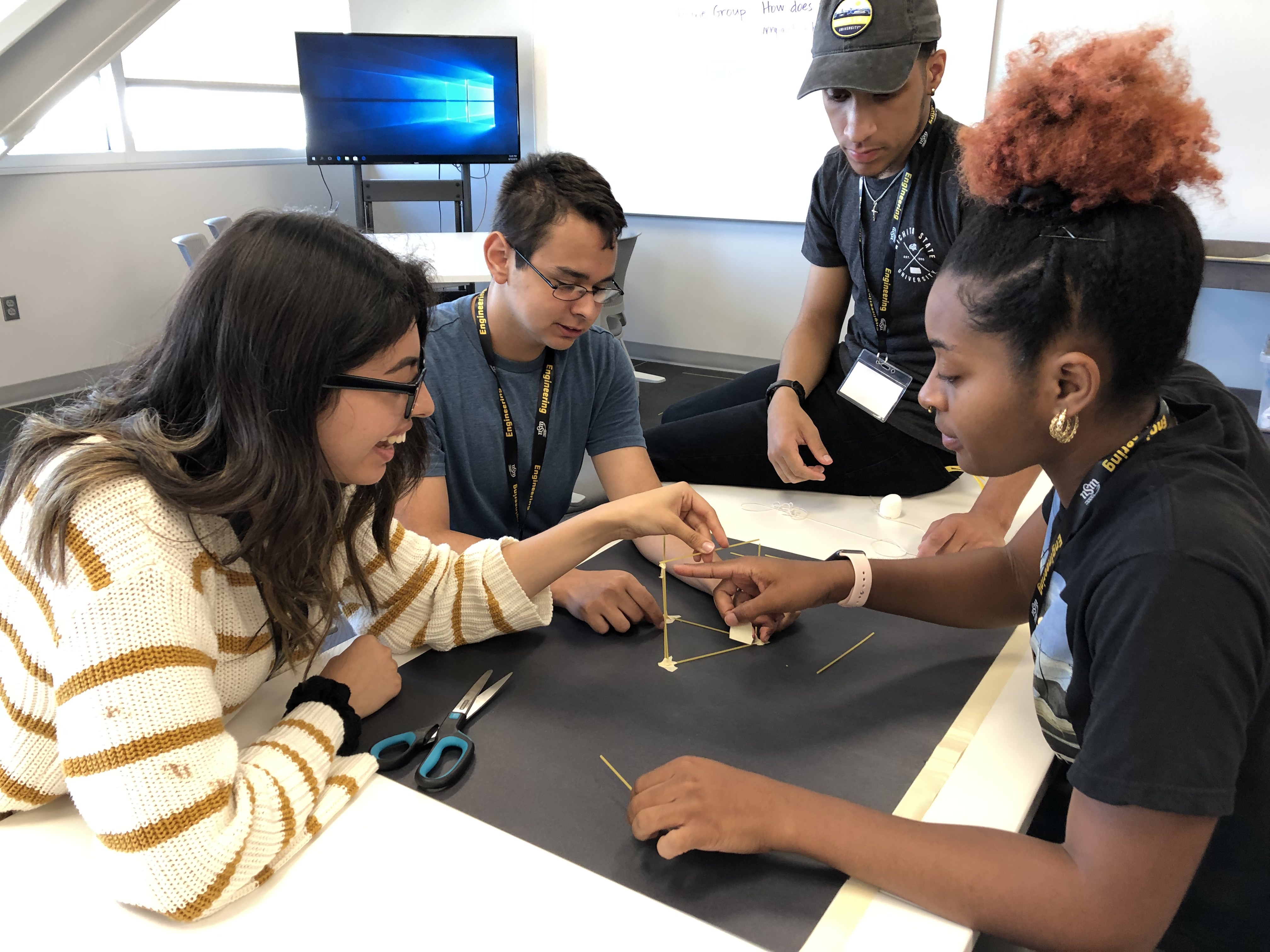 Four students build a tower with dry spaghetti.
