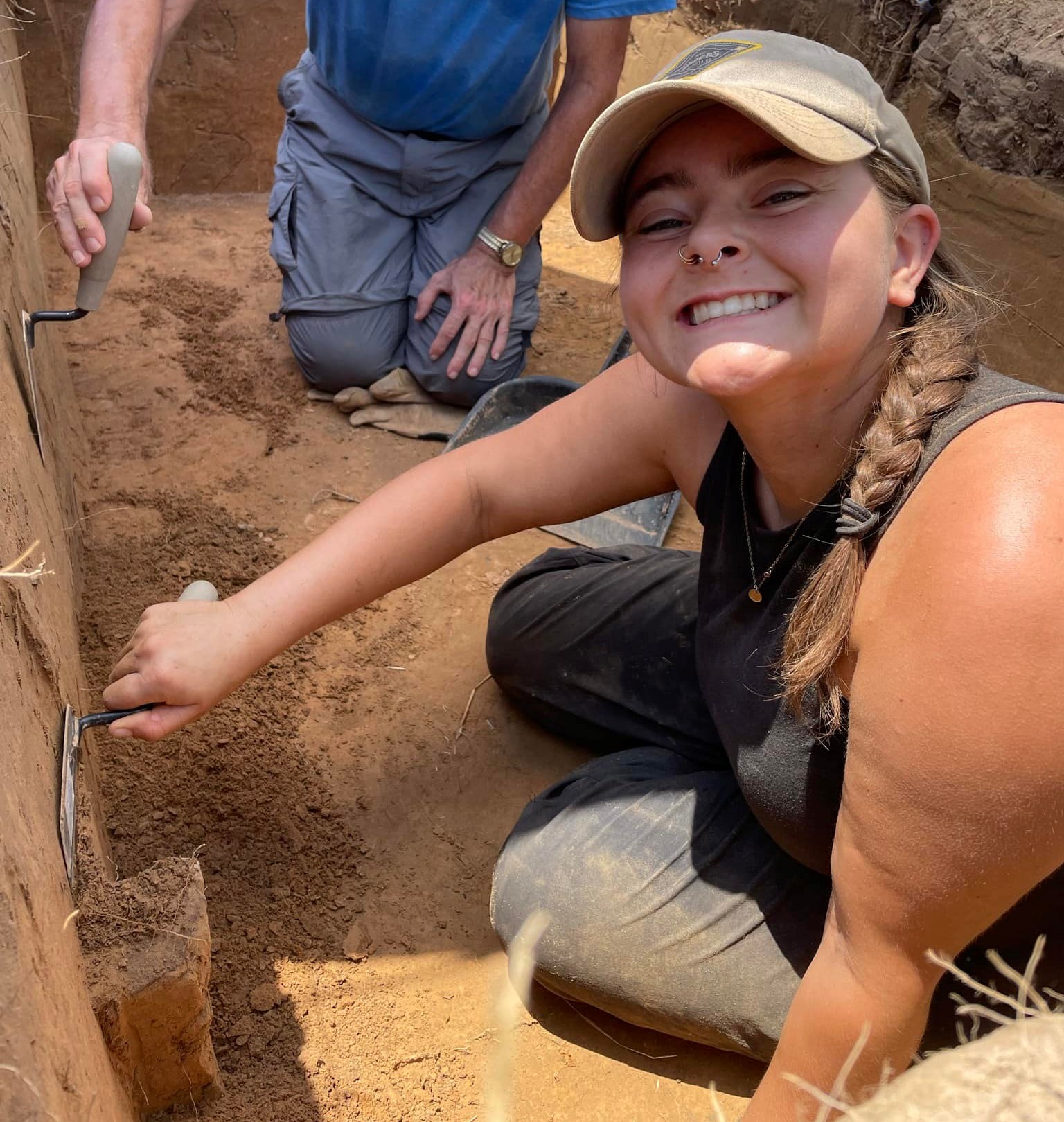 girl with nose ring smiling, holding trowel in earthen pit