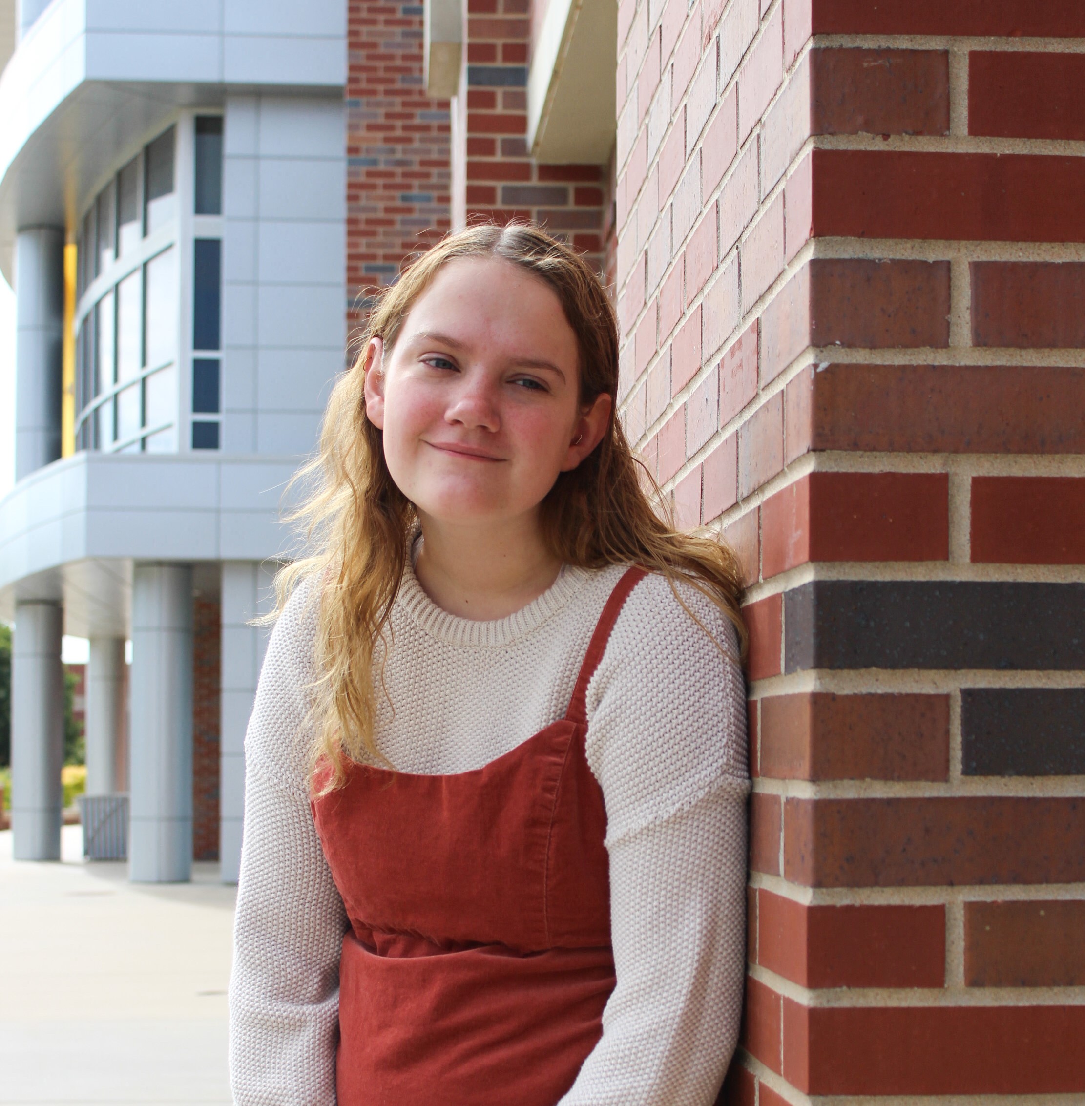 woman with blonde hair looks off camera in front of brick building